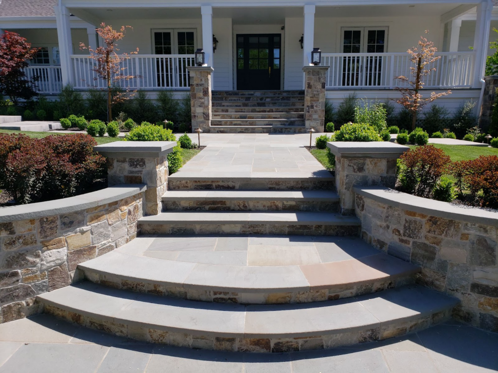 A pathway made from natural stone pavers in various sizes and shapes, leading to an outdoor seating area and fire pit surrounded by lush greenery.