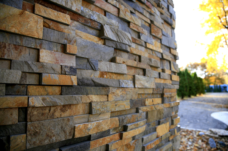 An exterior wall clad in natural thin veneer Fond Du Lac stone, showcasing a seamless blend of light cream, white, and soft gray stones. The precise installation reveals the stones' varied shapes and sizes, creating a sophisticated and elegant facade that enhances the building's architectural beauty. The sunlight gently highlights the texture and color variations of the stone, adding depth and character to the exterior.