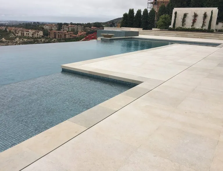 Stunning dual-design pool with soft limestone coping on one side and a dramatic infinity edge on the other, blending luxury and modern aesthetics.