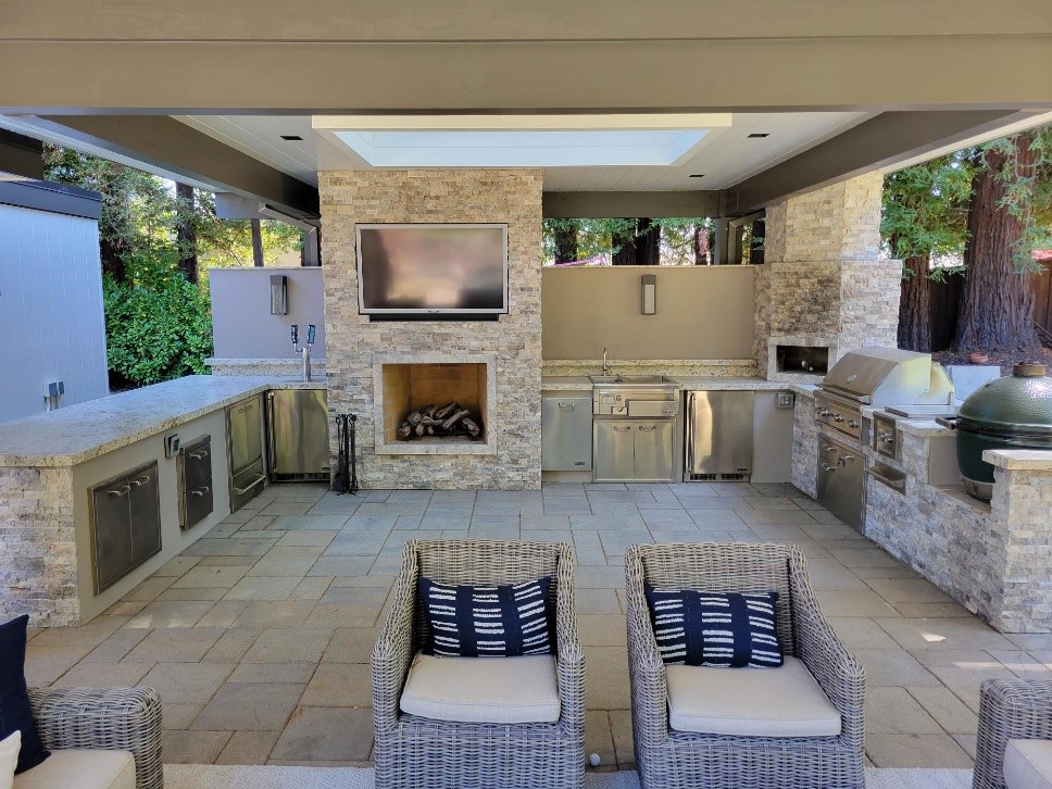 Luxurious covered outdoor kitchen and fireplace with stone veneer, built-in grill, and elegant patio seating, perfect for entertaining.