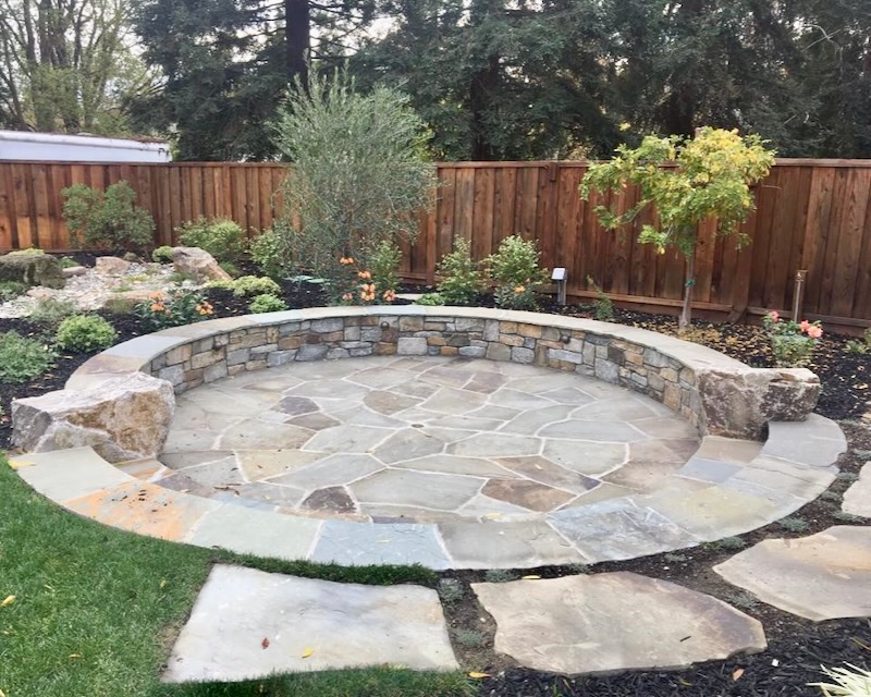 Circular sunken flagstone patio with a low surrounding wall, offering a secluded and intimate outdoor seating area.