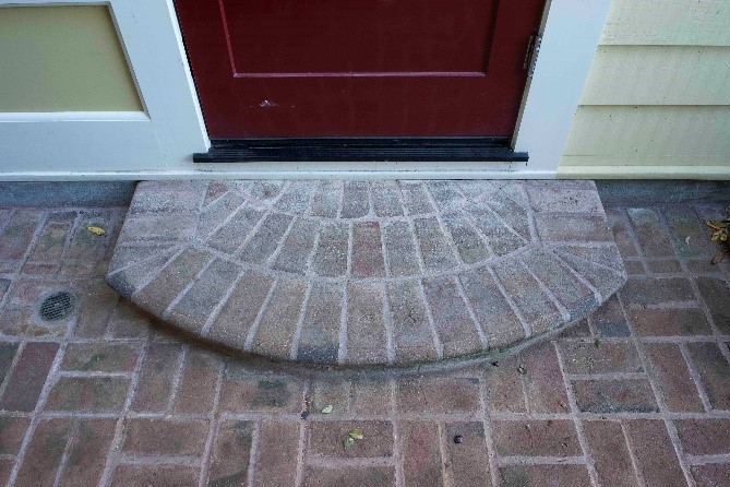 A semicircular brick paver step leading to a red front door, seamlessly blending with the surrounding brick patio.