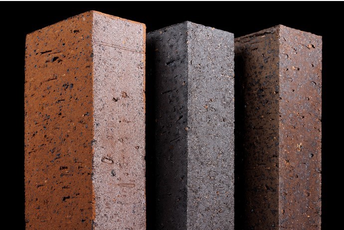 Close-up view of three vertical brick pavers in shades of red, dark gray, and brown, highlighting their surface textures and rich natural hues.