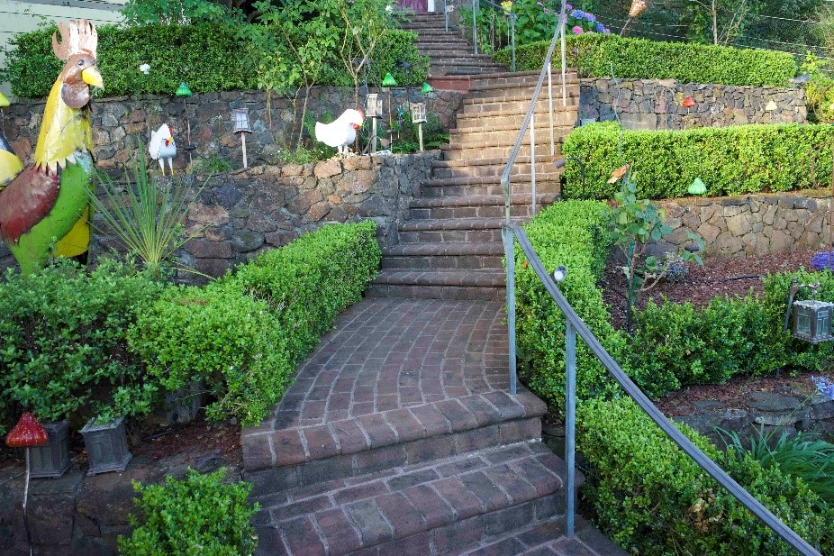 A scenic outdoor staircase made of red brick pavers, surrounded by lush greenery and colorful garden decorations.