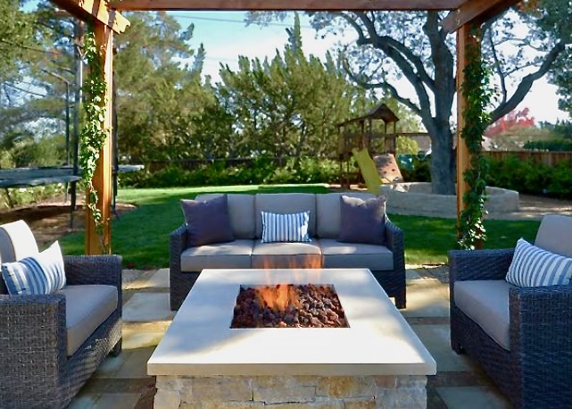 Charming outdoor firepit with a natural stone slab cap, surrounded by cozy seating under a pergola in a serene garden setting.