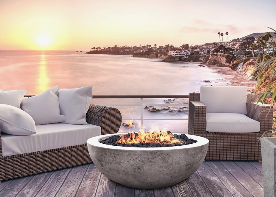 Modern outdoor patio with a stylish concrete fire bowl, wicker furniture, and breathtaking ocean sunset views. Perfect for luxury backyard retreats.