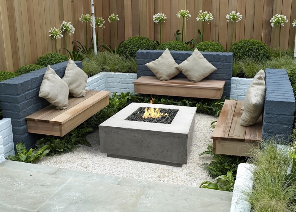 Modern outdoor seating area featuring a minimalist fire pit surrounded by built-in wooden benches and lush greenery for a cozy ambiance.