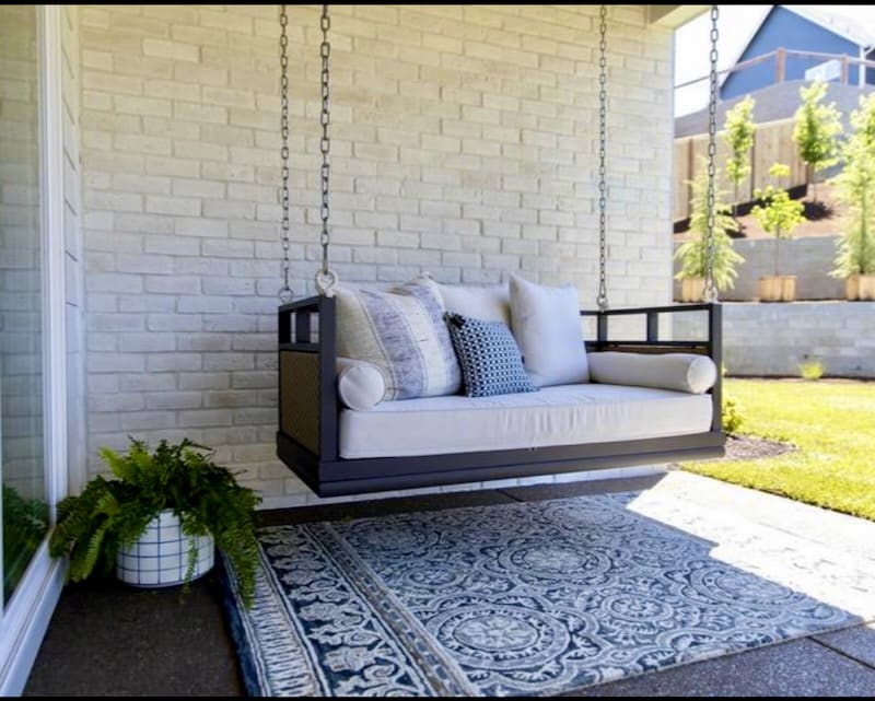 A cozy outdoor space with a black metal-framed swinging chair, set against a white brick wall for a relaxed and inviting atmosphere.