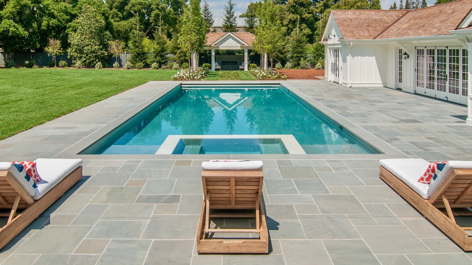 A stunning backyard retreat with a bluestone pool deck, crystal-clear water, and inviting lounge chairs, perfect for luxury outdoor living.