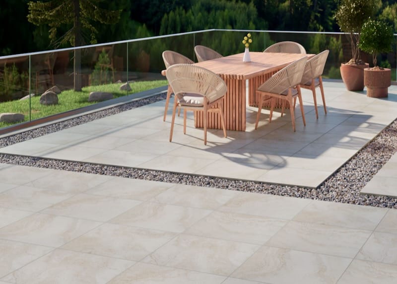 A modern outdoor dining space with light-colored porcelain pavers and a wooden table, showcasing fire-resistant and stylish paving solutions.