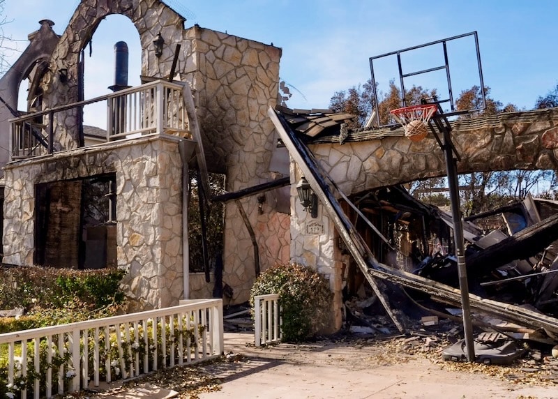 A fire-damaged home with stone veneer walls still standing, illustrating the resilience of fire-resistant building materials in wildfire-prone areas.