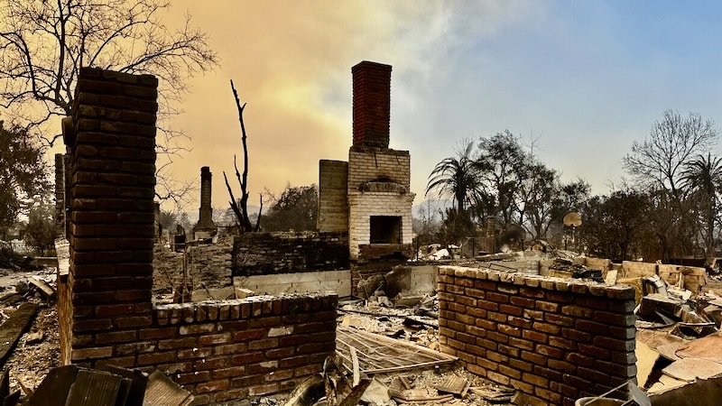 The aftermath of a wildfire showing a burnt-down neighborhood with only brick chimneys and stone walls remaining, highlighting the importance of fire-resistant materials.