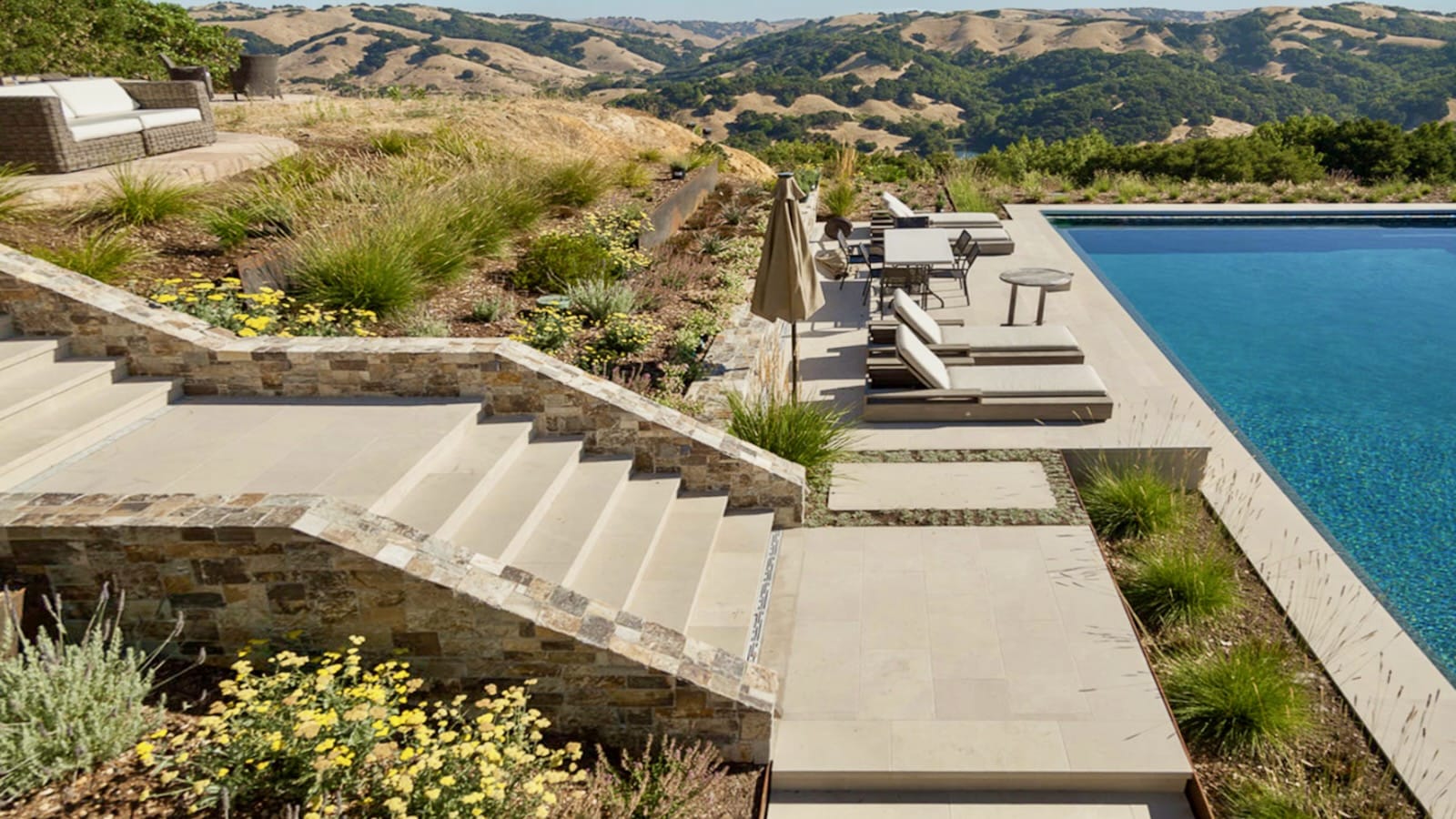 A breathtaking hillside poolside retreat featuring a custom natural stone patio, stunning valley views, and resort-style seating.