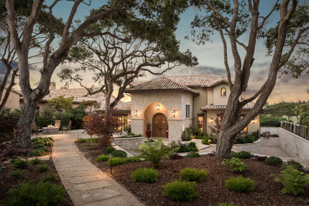 Mediterranean-style home in Monterey, CA, using clay tile roofing, arched stone entryway, and lush landscaping to blend timeless design with natural materials.