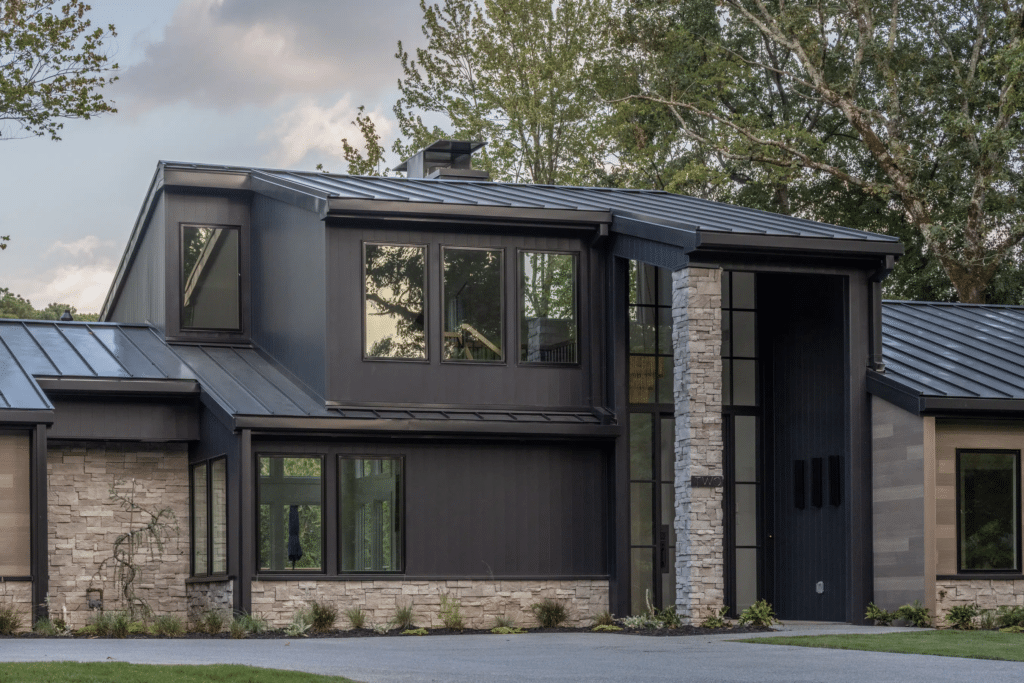 Modern farmhouse-style home with dark metal siding, vertical wood accents, and natural stone veneer, highlighting a popular combination for 2025 exteriors.