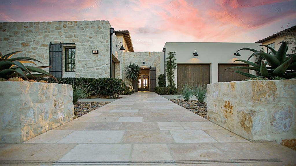 California ranch-style home entrance with limestone exterior, dark wood garage doors, and desert-friendly landscaping, illustrating a rustic-modern blend.