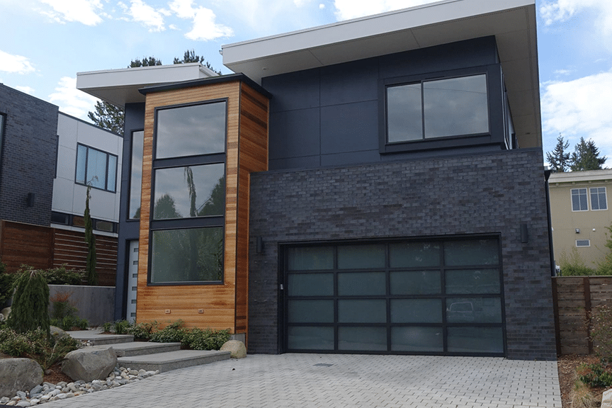 Contemporary home facade combining dark brick, cedar wood siding, and black-framed windows, showcasing the 2025 mixed materials trend.