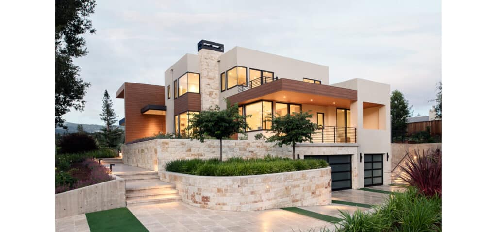 Modern Bay Area home exterior featuring mixed materials, including natural stone walls, wood paneling, and stucco, with elevated landscaping and lighting.