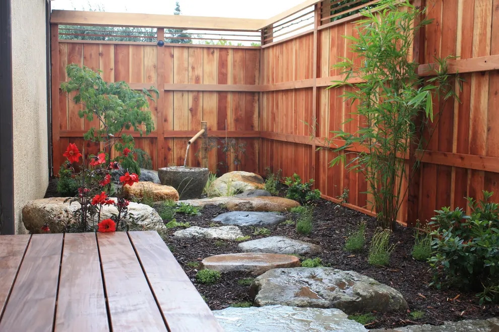 Natural stone pathway with water feature and lush greenery in a small Bay Area backyard.