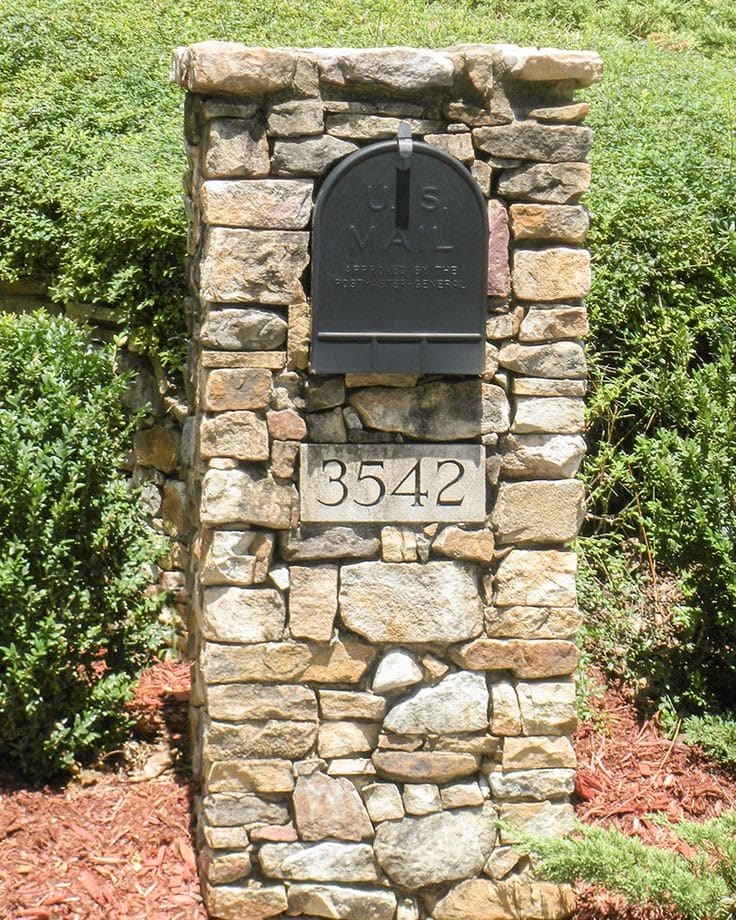 Stacked fieldstone mailbox column with black metal mailbox and engraved house number plaque.
