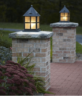 Brick columns with lantern-style lights illuminating a red brick pathway at dusk.