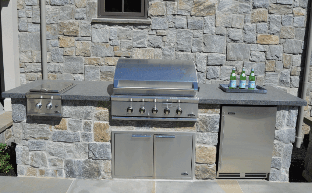 Outdoor kitchen with stainless steel grill and stacked stone veneer wall.