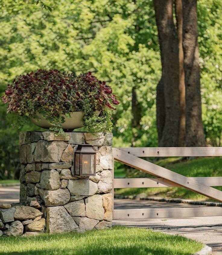 Natural stone mailbox post with planter and lantern light, next to a rustic wood gate.