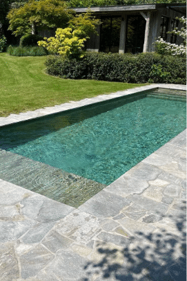 Swimming pool surrounded by a light-colored flagstone pool deck and green landscaping.