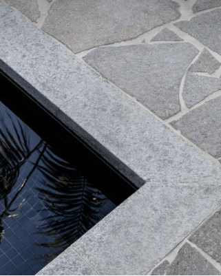 Left, close-up of pool edge): Close-up of a pool coping and deck using large-format grey flagstone for a sleek, non-slip surface.