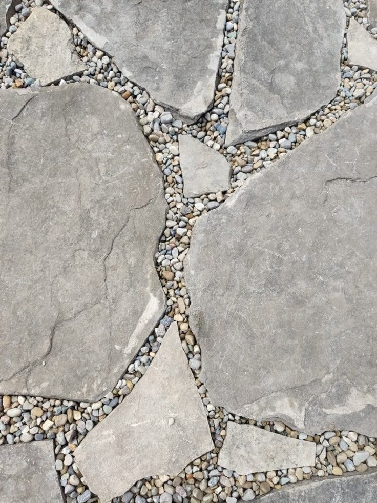 Grey irregular flagstone paving stones separated by small river pebbles, showcasing a detailed hardscaping texture.
