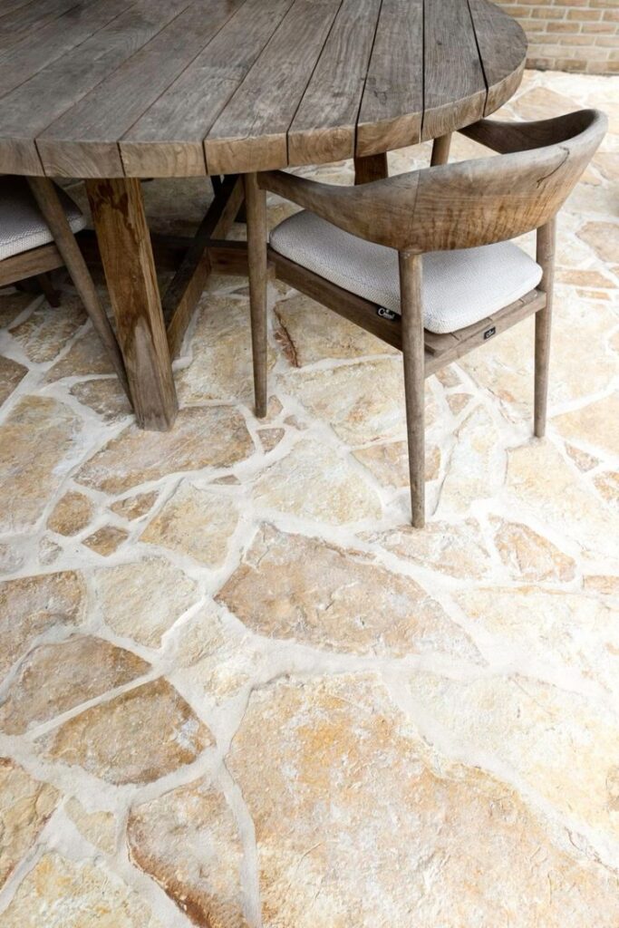 Warm-toned irregular flagstone patio flooring with rustic wooden table and chairs, ideal for outdoor living design.
