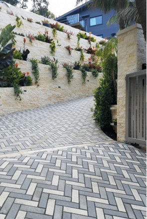 Herringbone paver pattern on a steep driveway bordered by terraced retaining walls and plantings.