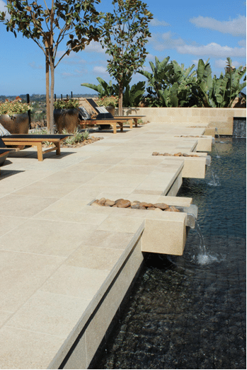 Light limestone pavers and coping forming a sleek pool deck with water features.