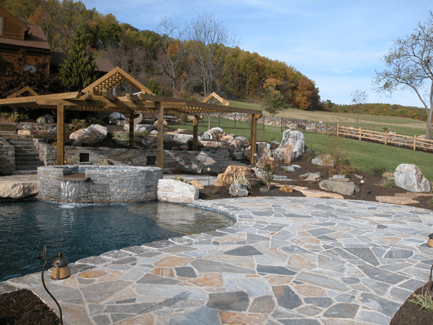 Flagstone patio design surrounding a pool with pergola and natural landscaping.