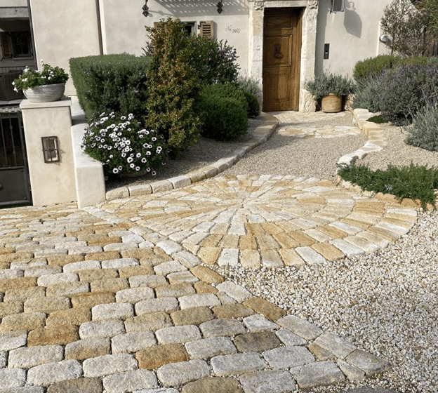 Charming cobblestone driveway and walkway with circular stone pattern leading to a rustic front door.