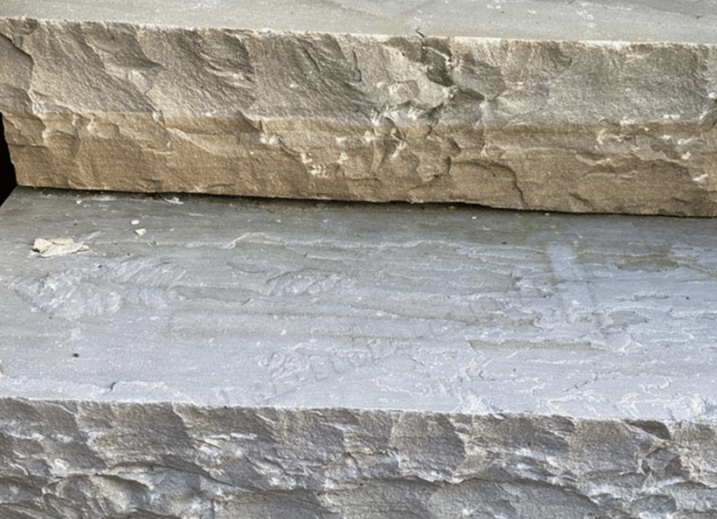 Close-up of thick stone steps with rough split-face risers and textured treads showing natural layers and chisel marks.