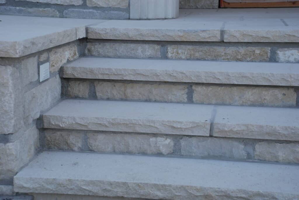 Exterior entry steps built with light stone treads and rough-faced stone risers creating a solid, traditional look.
