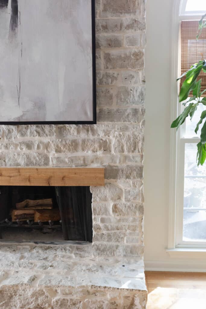 Interior fireplace clad in light textured stone with a simple wood mantel and contemporary artwork above.