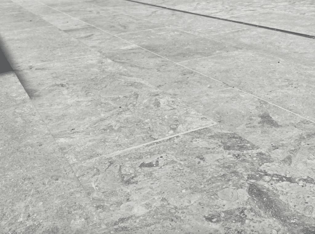 Close-up of gray stone paving with subtle veining and fossil-like markings across the honed surface.