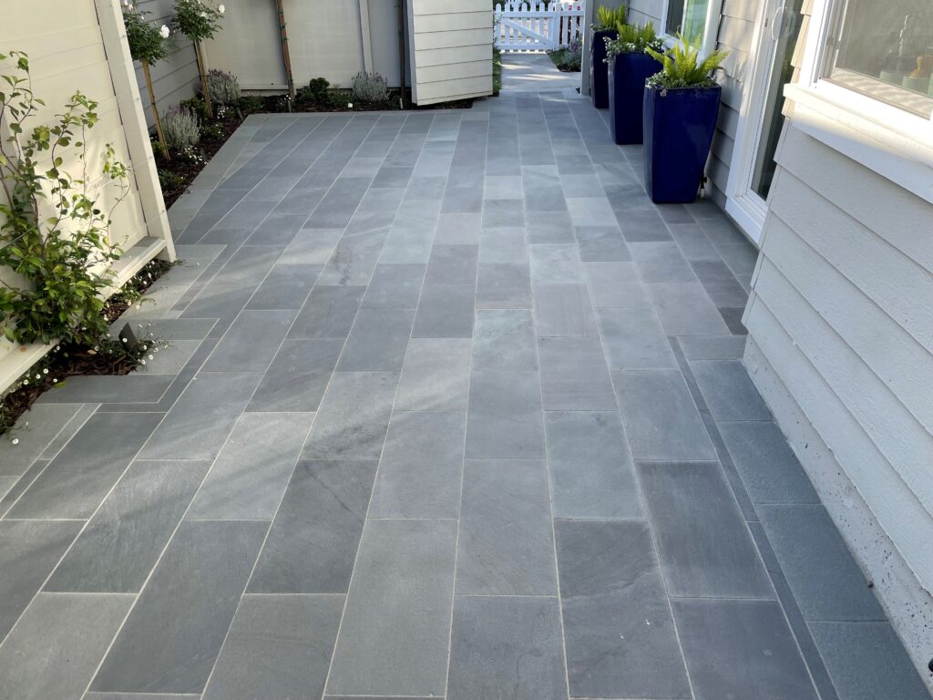 Narrow courtyard paved with long rectangular gray stone pavers laid in a modern running bond pattern beside a home.