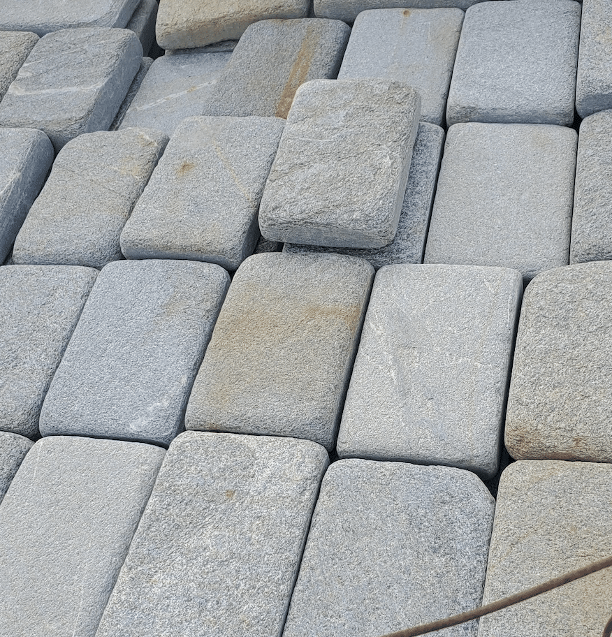 Sydney Peak tumbled cobbles stacked in mixed sizes – Assorted Sydney Peak cobblestones in soft grey tones with rounded, tumbled edges, shown piled/stacked for paving applications.