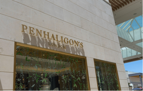 Retail storefront clad in smooth cream-colored stone panels with gold PENHALIGON'S LONDON signage above large display windows.