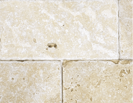 Cream tumbled stone tiles with softened edges and light surface pitting laid in a running bond pattern.
