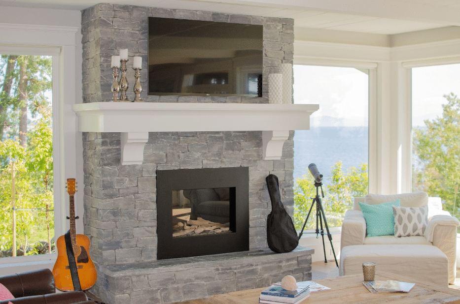 Ocean Pearl stacked stone veneer fireplace with white mantel and mounted TV in a coastal-modern living room with Bay view windows.